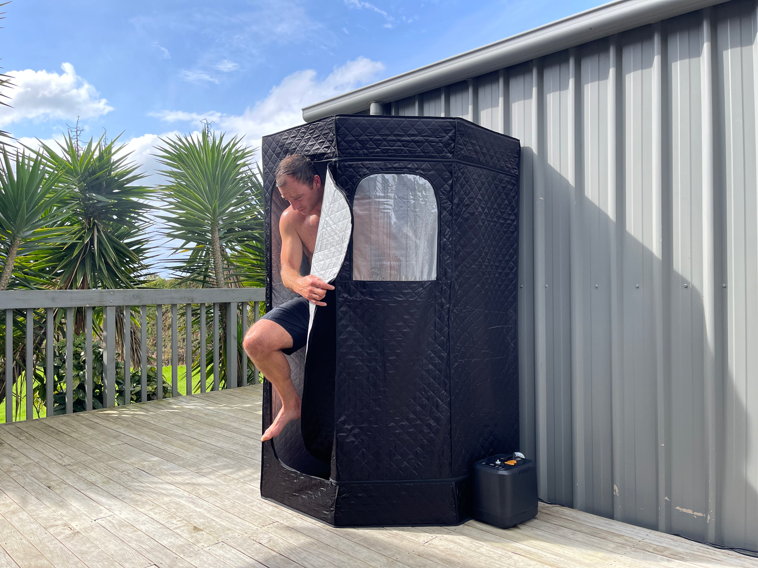 Person using a portable shower pod on a deck with a scenic background
